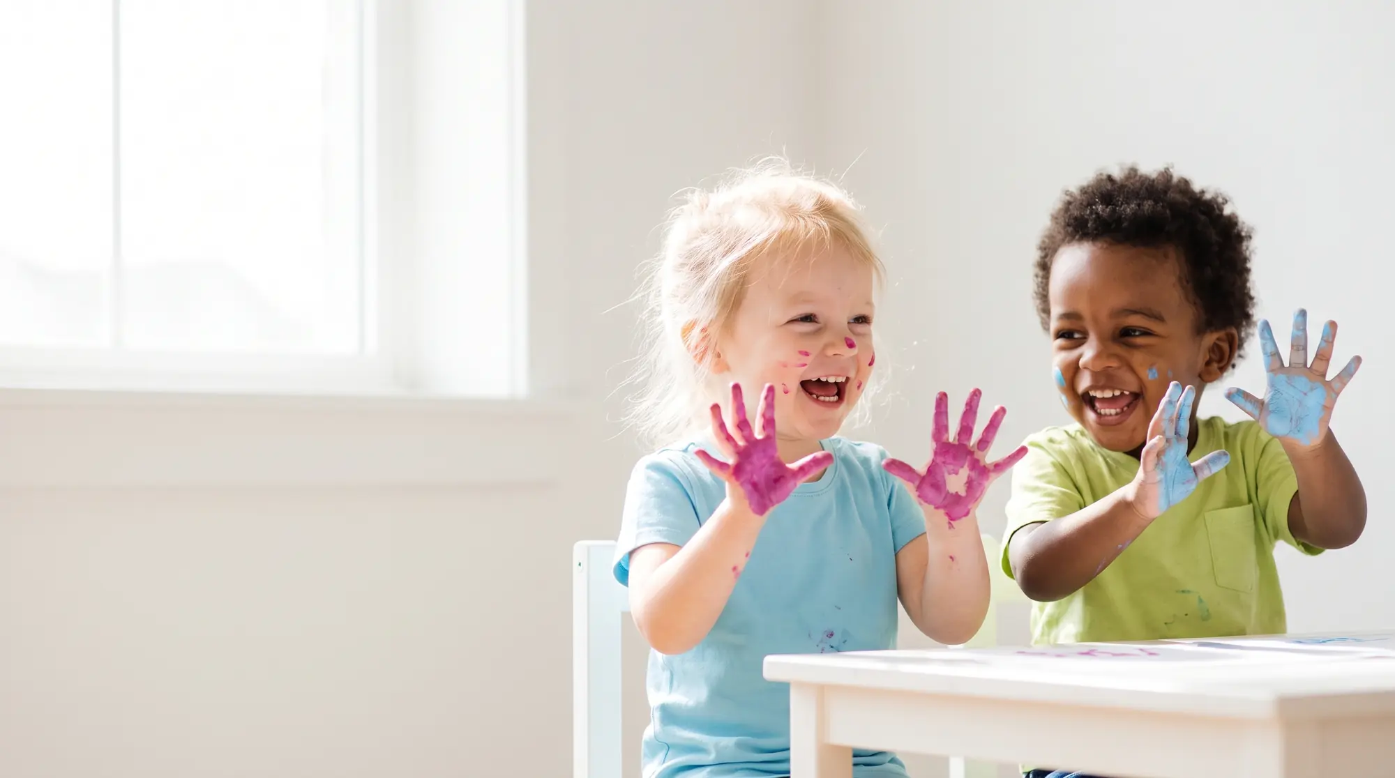 Two smiling toddlers holding up their painted hands